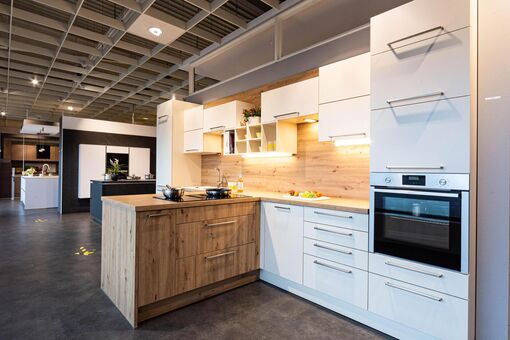 Die Kombination aus weißen Oberflächen und Holzfronten greift die Form der Küche auf und erzeugt so ein harmonisches Bild